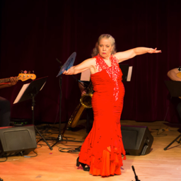 Aurora Reyes, red sleeveless flamenco dress, arms extended side to side, 3 musicians in background.